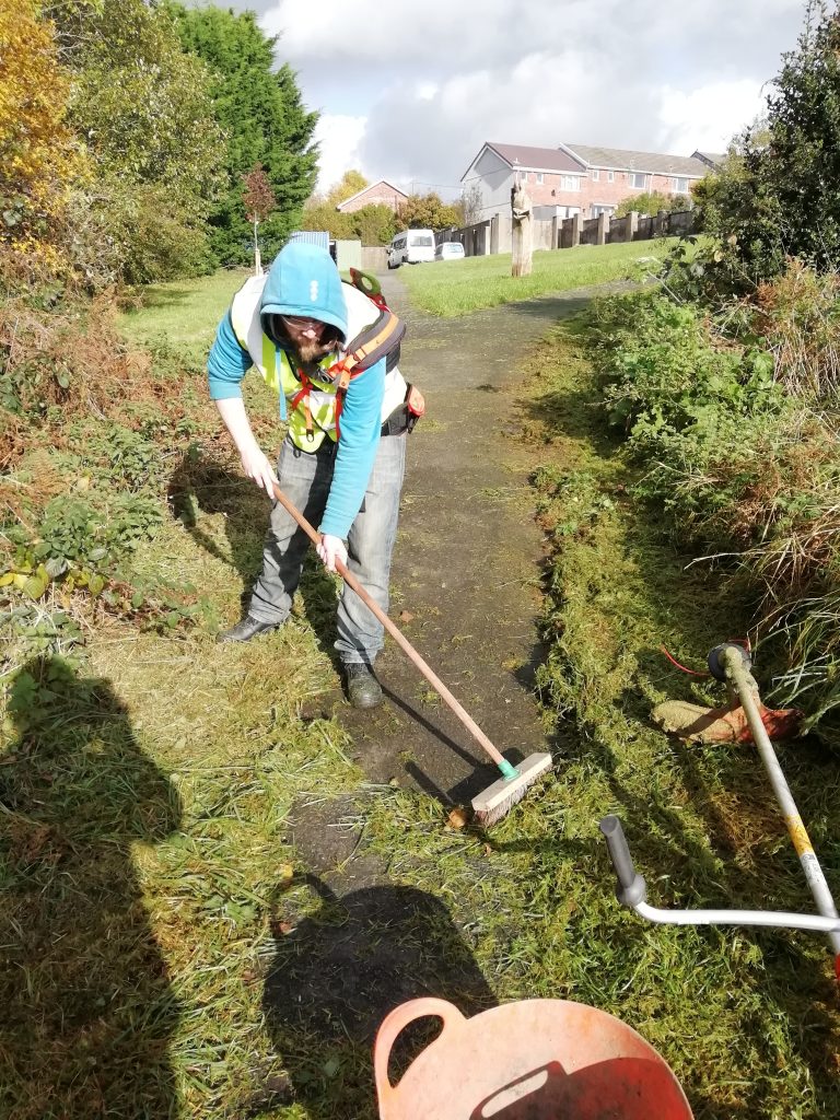 Greencare Team Member sweeping a recently strimmed path.