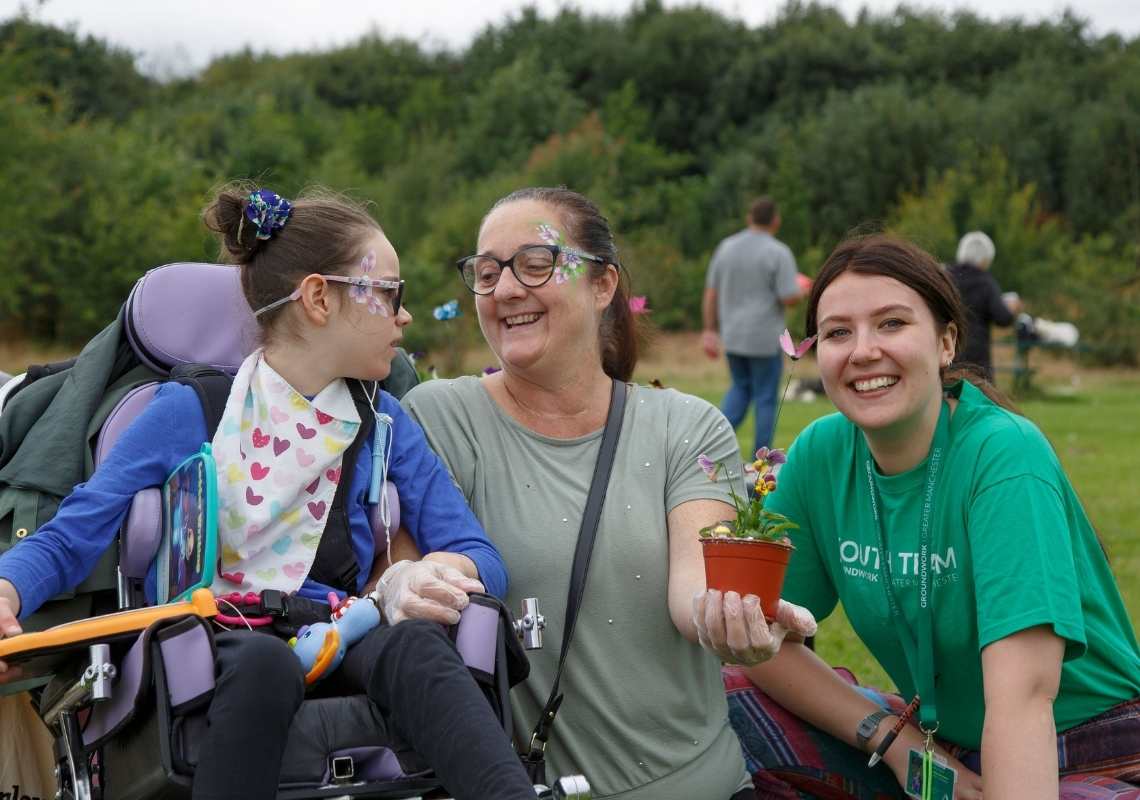 A young girl in a wheelchair having fun in green space with two adult women