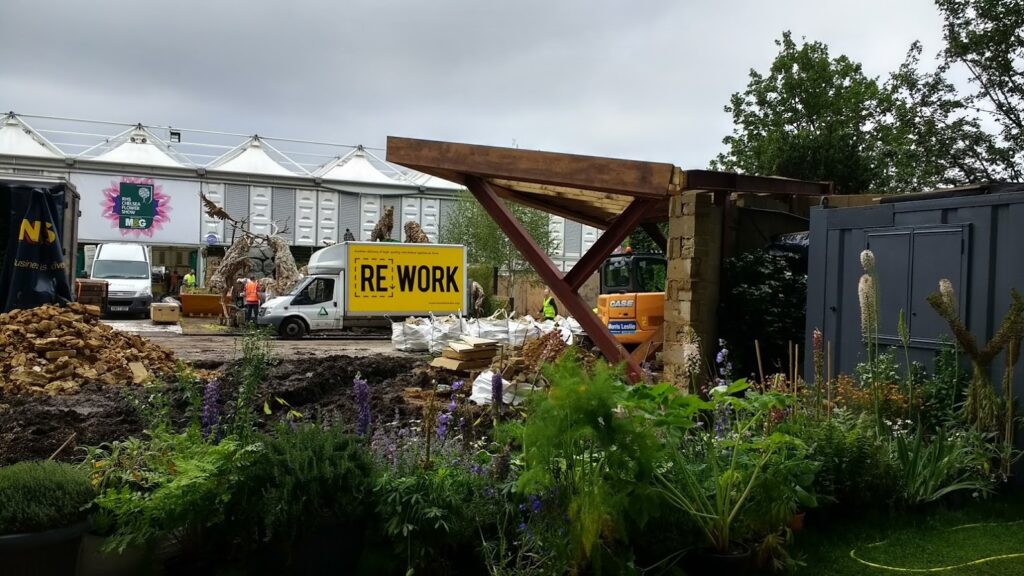 A yellow 'Rework' branded van parked in a yard of bricks and flower beds.