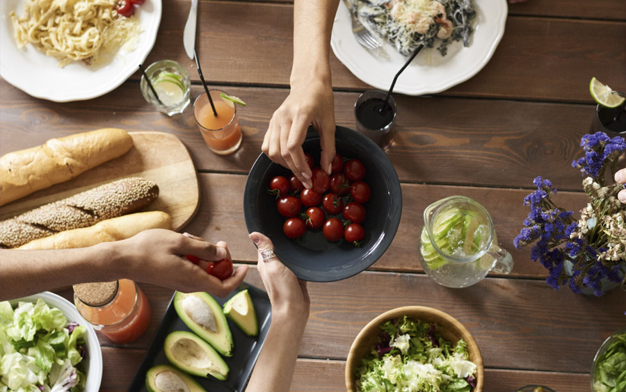People sharing healthy meal on wooden table with various fresh produce and food.