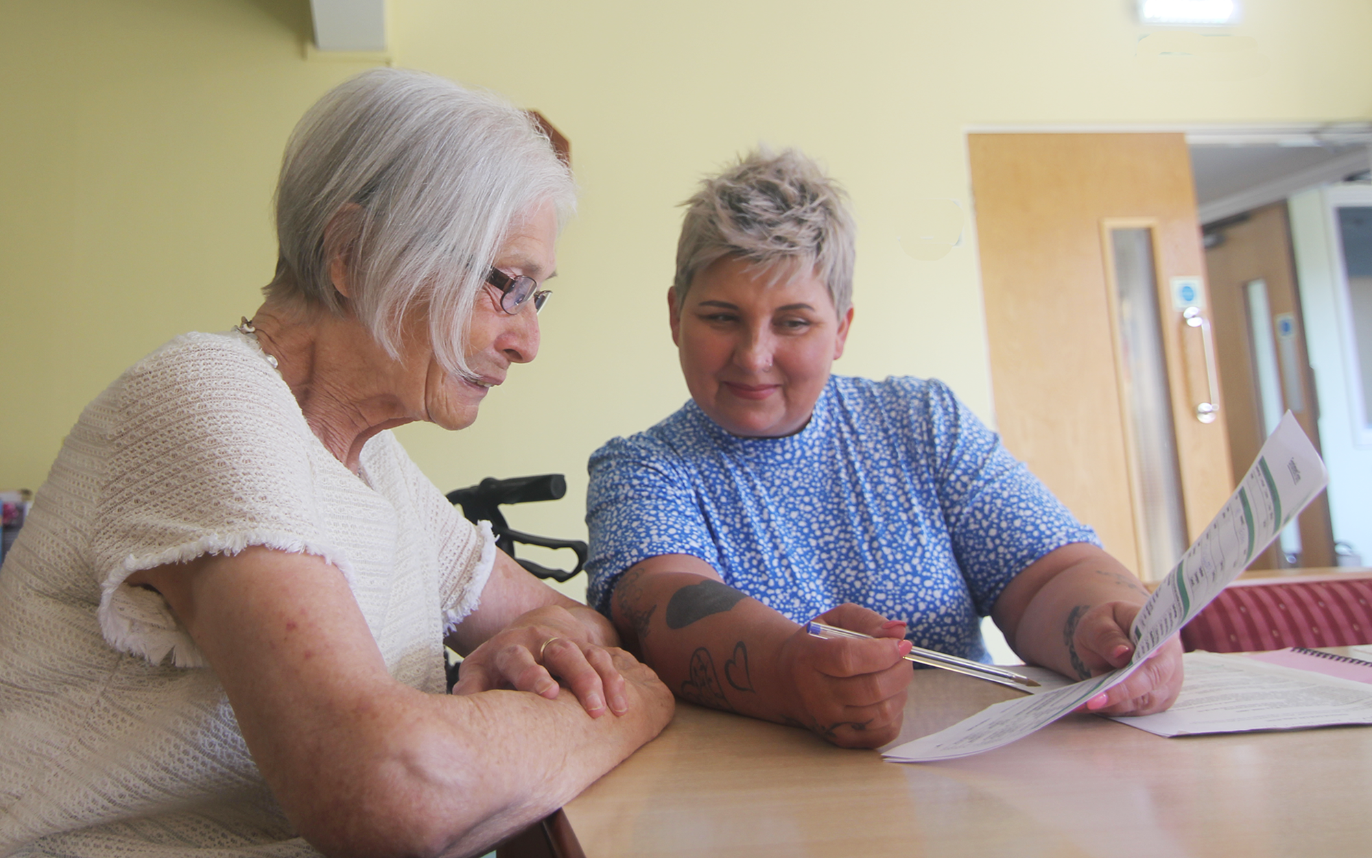 Two women at table looking at paper.