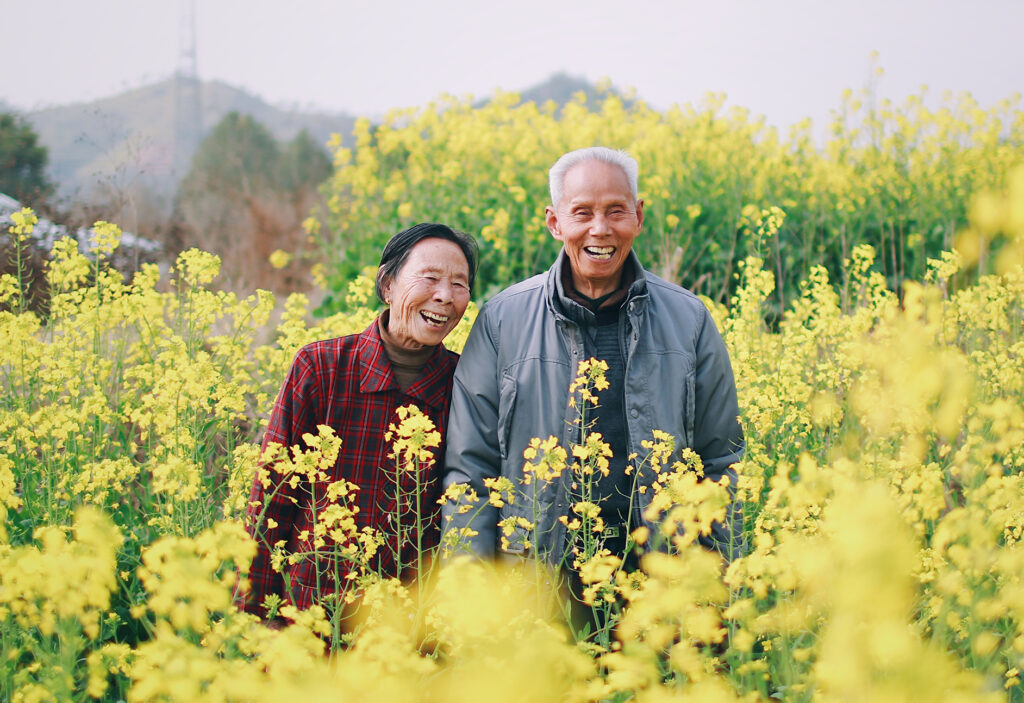 Happy Asian couple standing in field with flowers