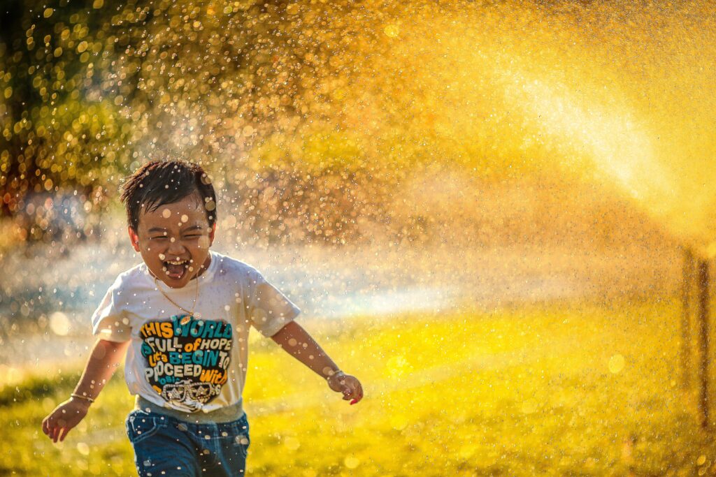 Young Asian boy running through sprinklers in golden sunset