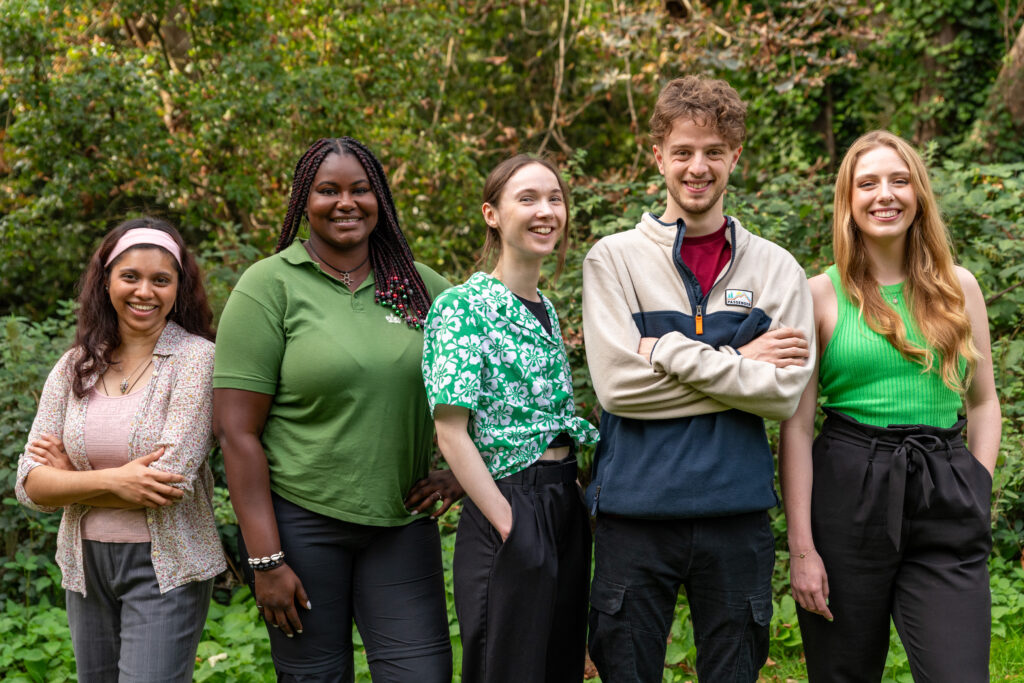 Image of new to nature trainees in london October 2023. Image shows 5 young people in a woodland area smiling at the camera.