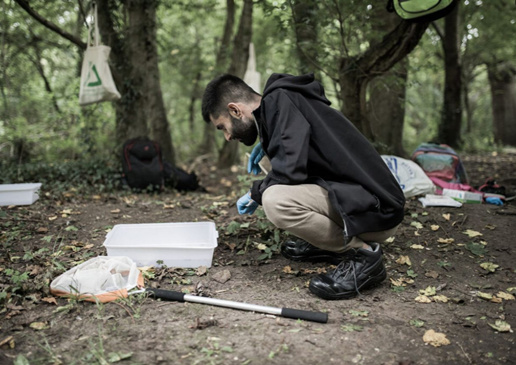 Photo of a young man kneeling down in a green space.