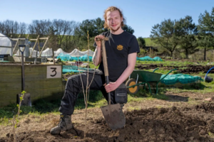 Photo of Ben in a garden centre kneeling down holding a shovel.