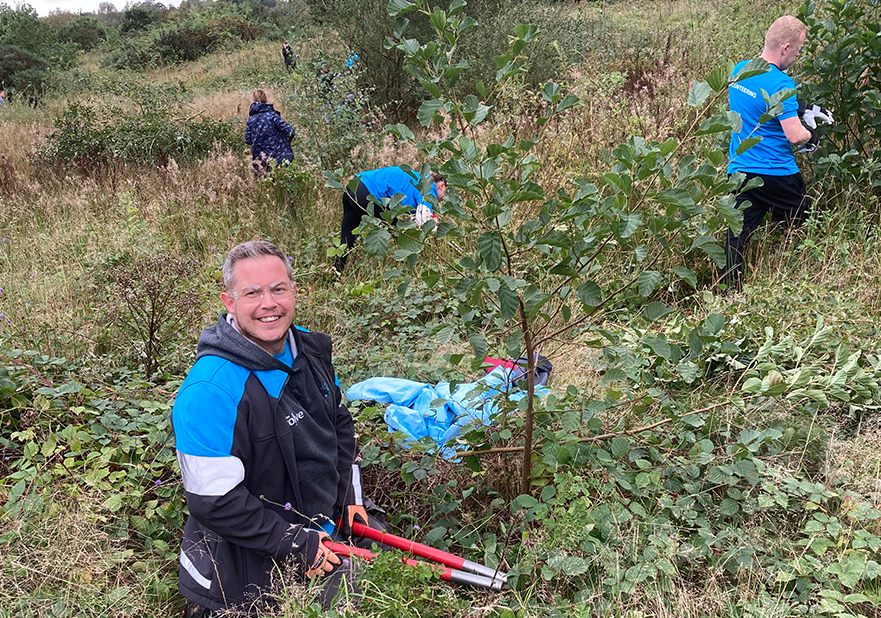 People in blue and black clothing working outdoors. One man looks at the camera, holding gardening tools.