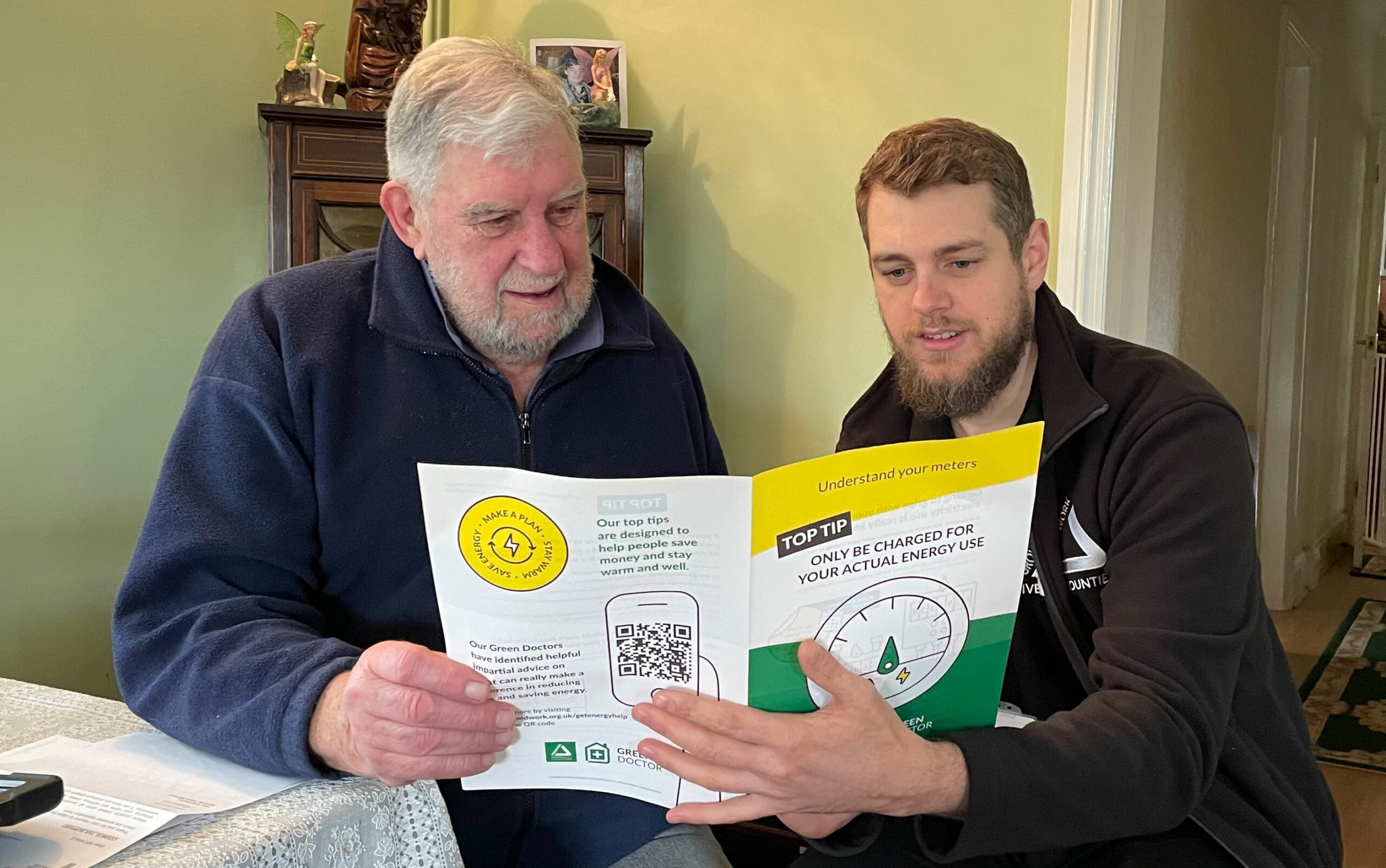 Two men, one elderly and the other young, looking at energy saving brochure, sitting at table.
