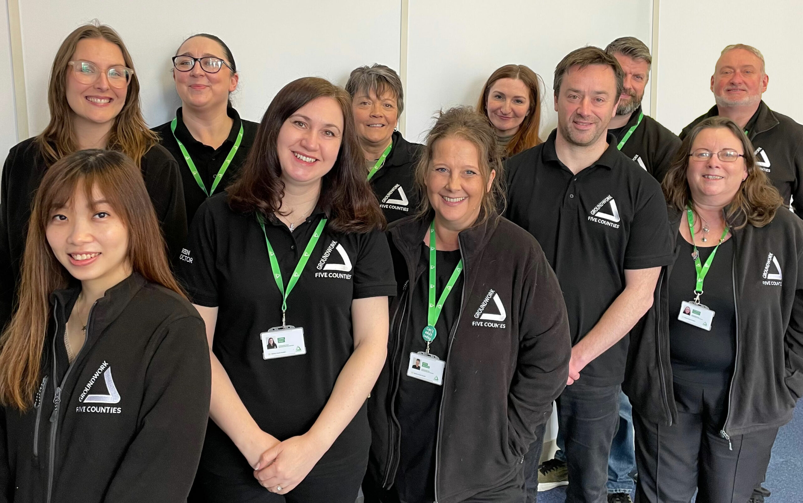 Group of people wearing black branded tops with white Groundwork logo, smiling at camera.