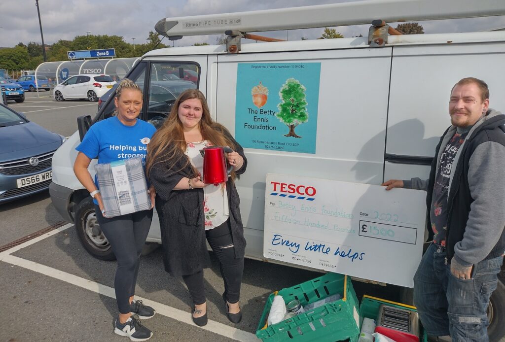 Three people standing in front of a van with a cheque in hand