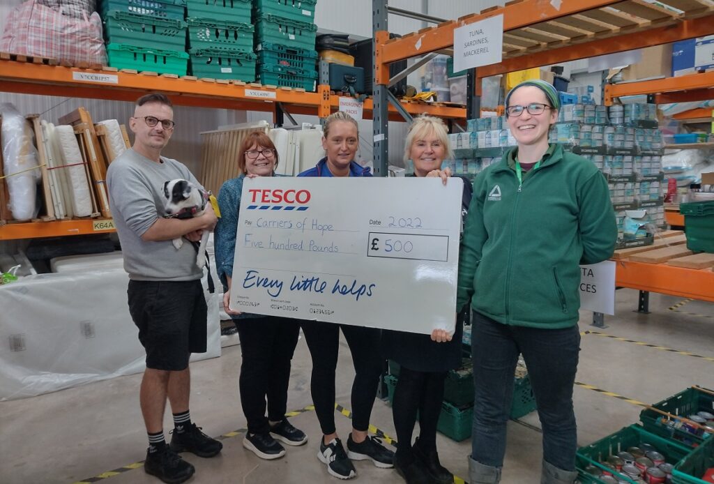 Four people in a warehouse holding a cheque