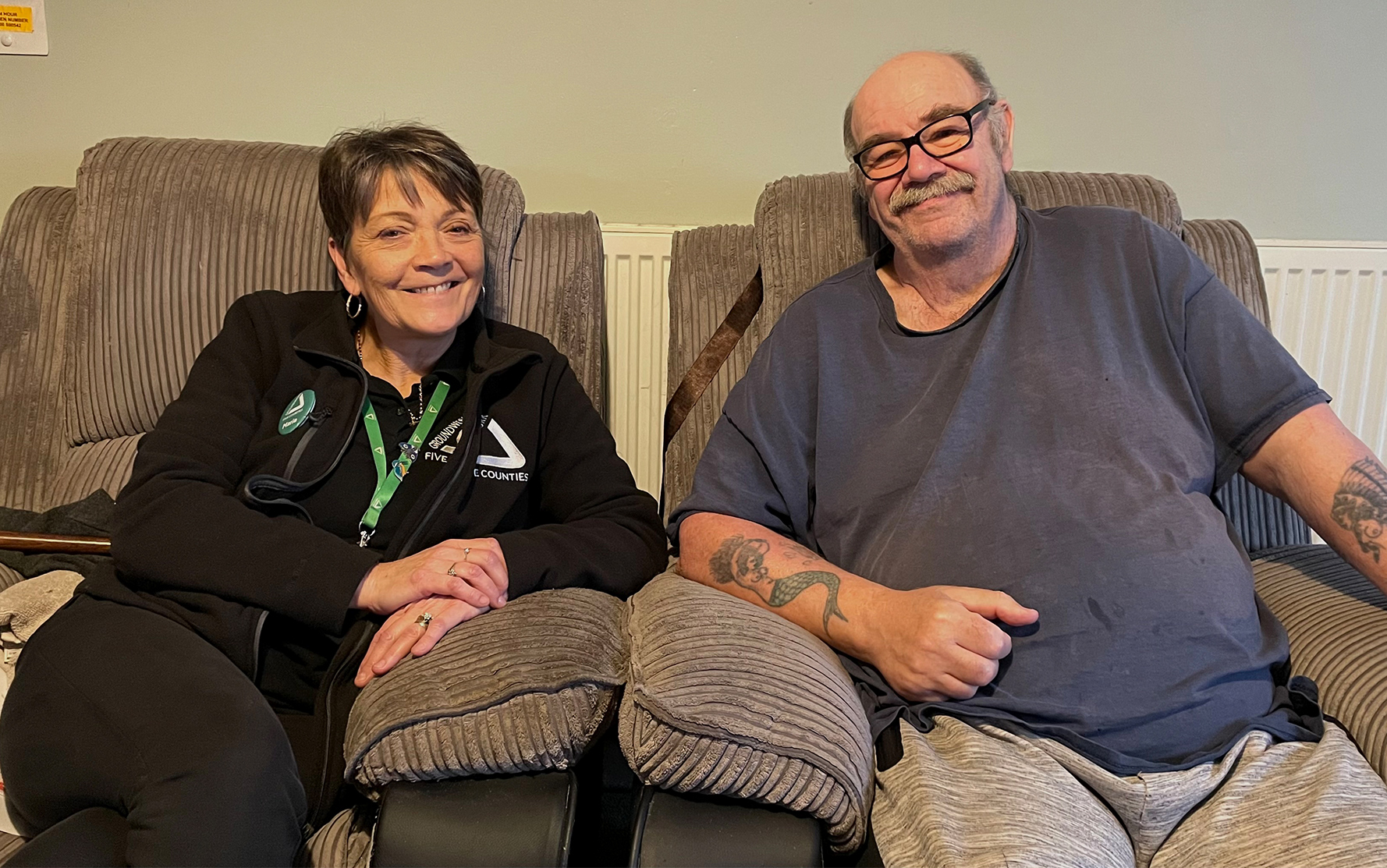 Man and woman sitting on grey comfy chairs smiling at camera.