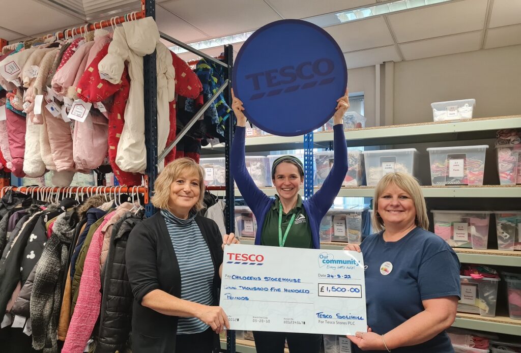 Two people holding a cheque and one person holding up a blue Tesco coin
