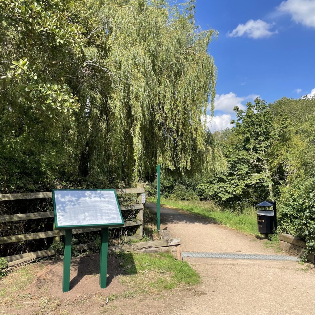 A noticeboard next to a path with green trees surrounding