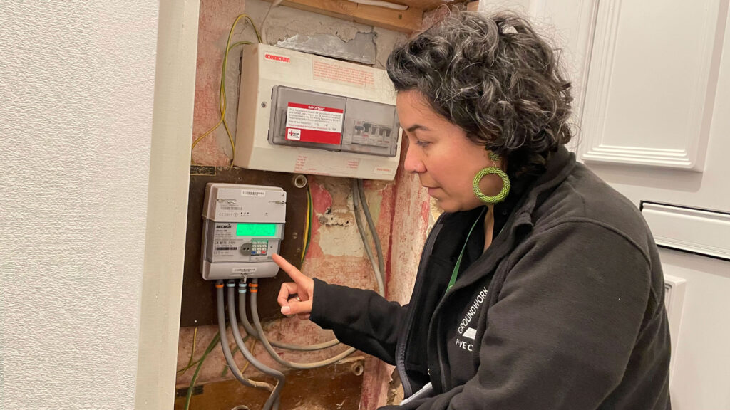 Dark haired woman wearing black fleece jacket with smart meter in cupboard.