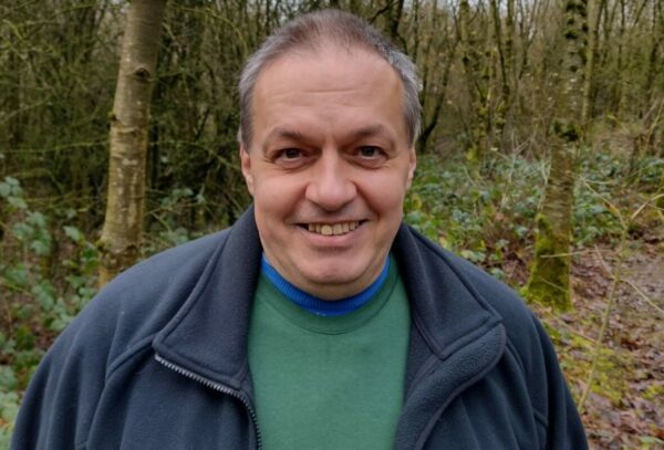 A man standing for a photo with trees and bushes growing in the background