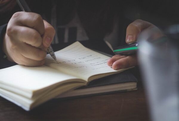 A person writing in a book with a pen and using a calculator 