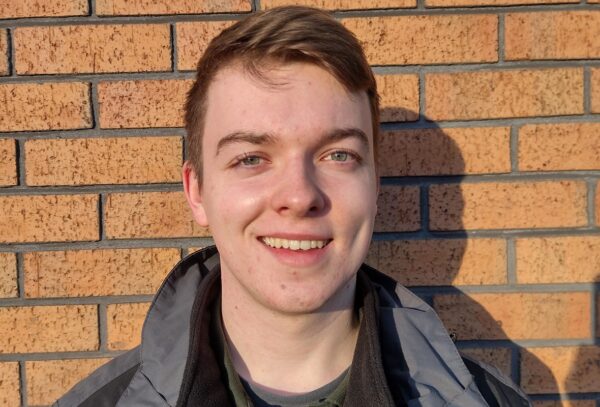 A young man standing for a photo in front of a brick wall