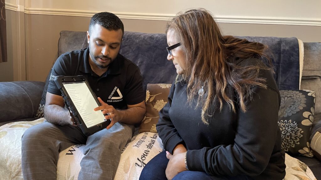 Man and woman sitting on sofa looking at information on a tablet device.