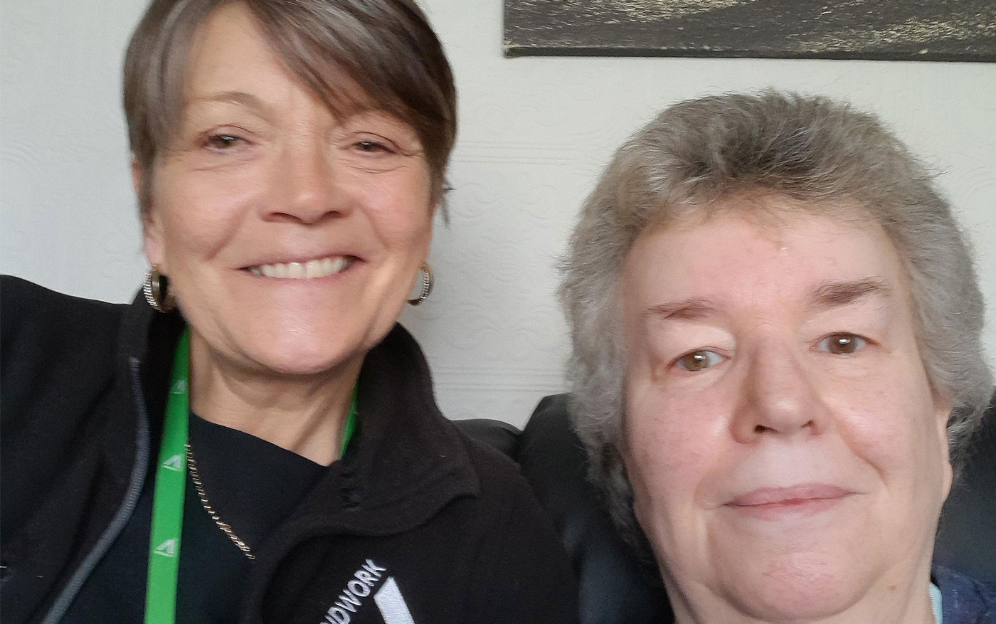 Two women smiling at the camera, the woman on the left wears a green lanyard.