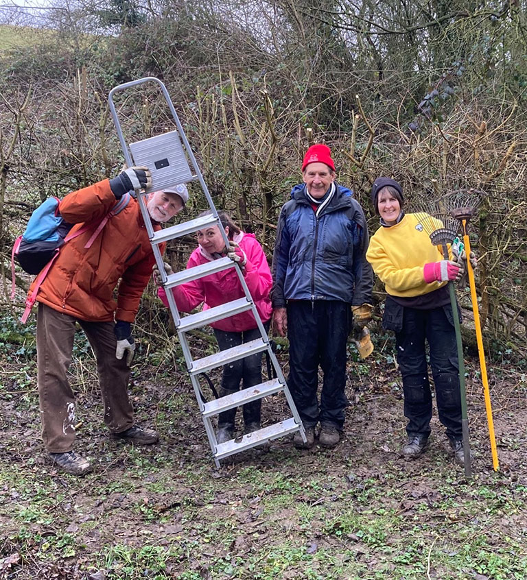 Group of people with ladder and rakes, smiling at the camera in outdoor setting