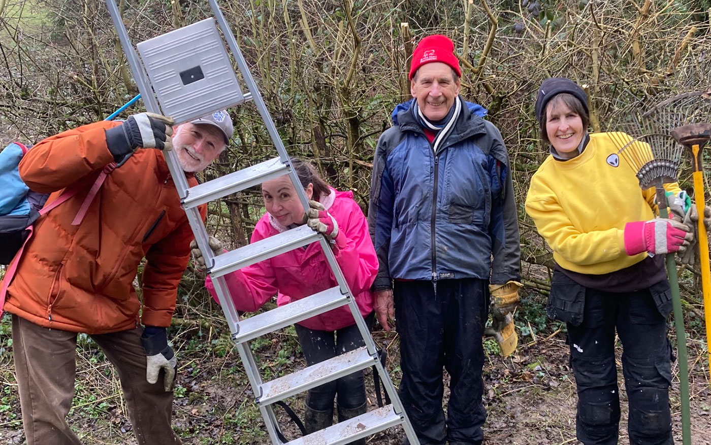 Group of people with ladder and rakes, smiling at the camera in outdoor setting