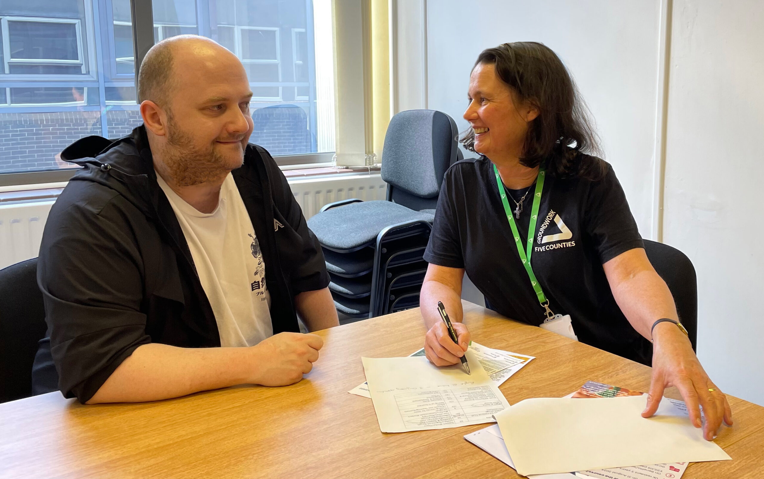 Man and woman sitting in office with papers on table, smiling at each other