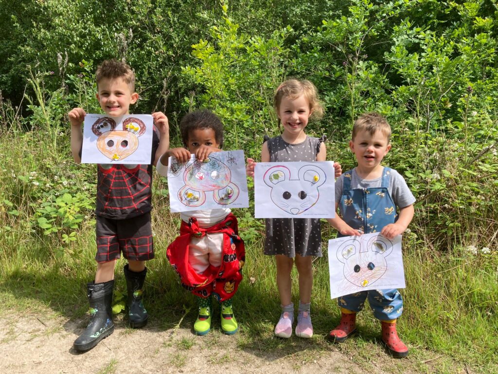 Four children of different ages holding colouring page with mouse, in outdoor setting.