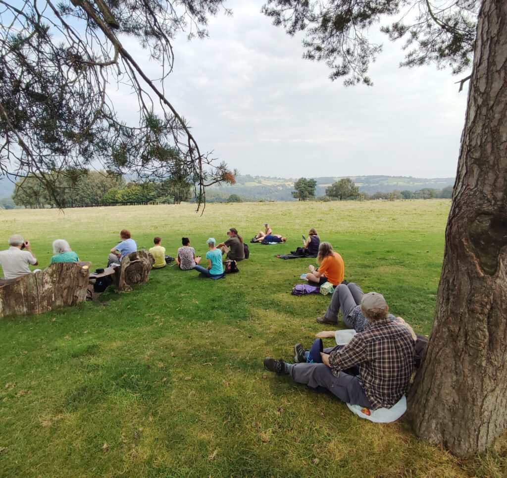 Group of people sitting on grass with view of rolling hills.