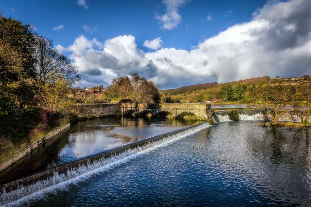Lake with dams, stone bridges, trees, and blue sky.