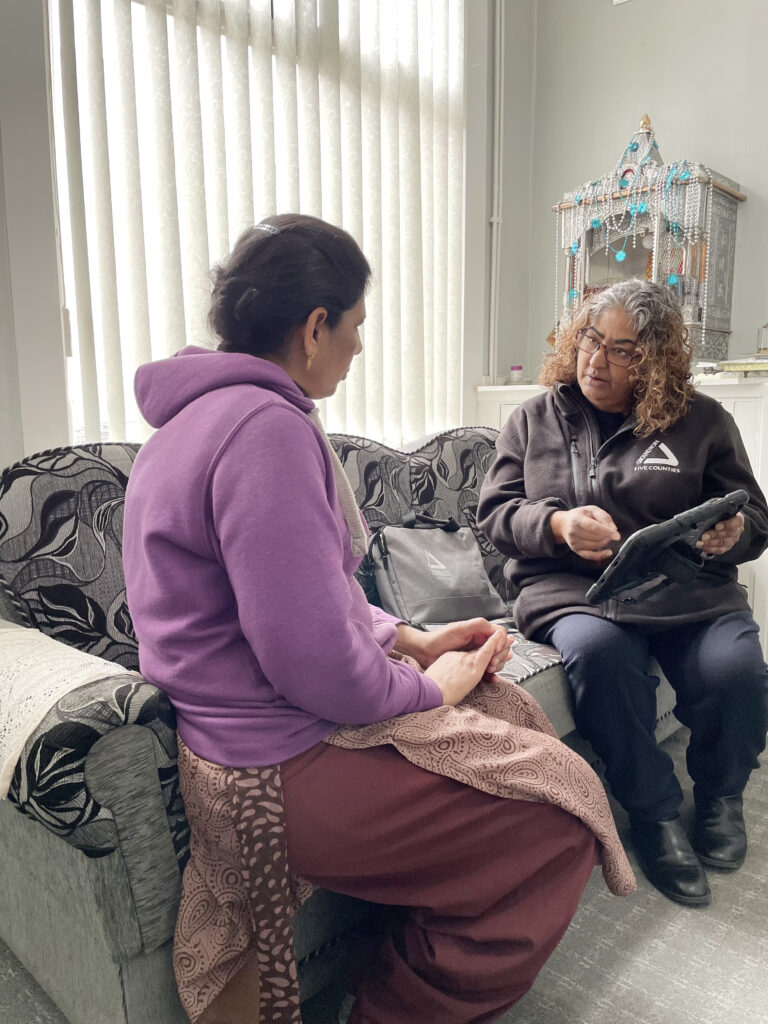 Two women sitting on sofa speaking. Woman in forefront wears a purple hoody, woman at the back wears a black fleece with white Groundwork logo.