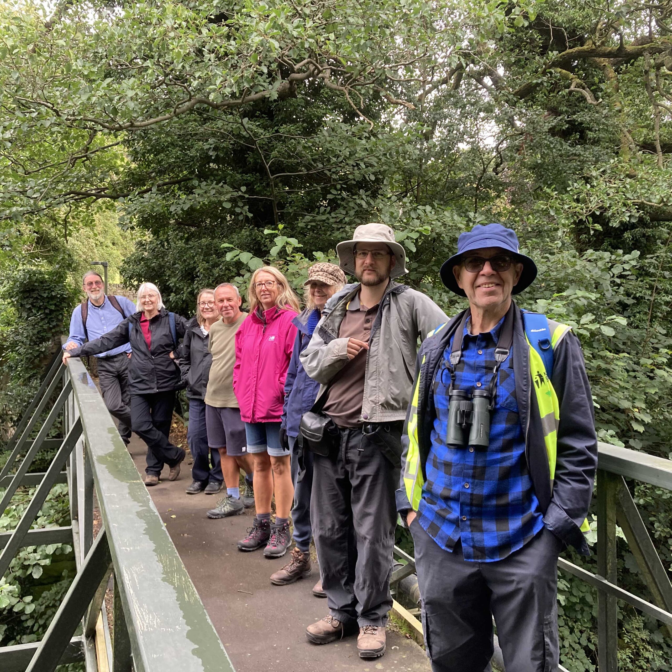 Group of people standing on bridge smiling at camera with trees in background.