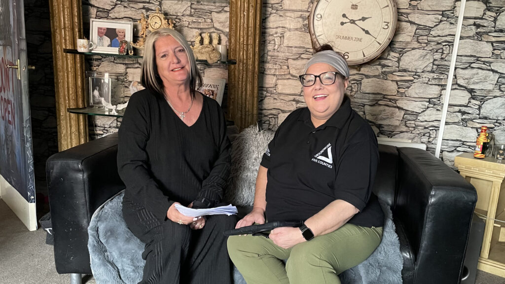 Two women sitting on a black leather sofa smiling at the camera in cosy living room.