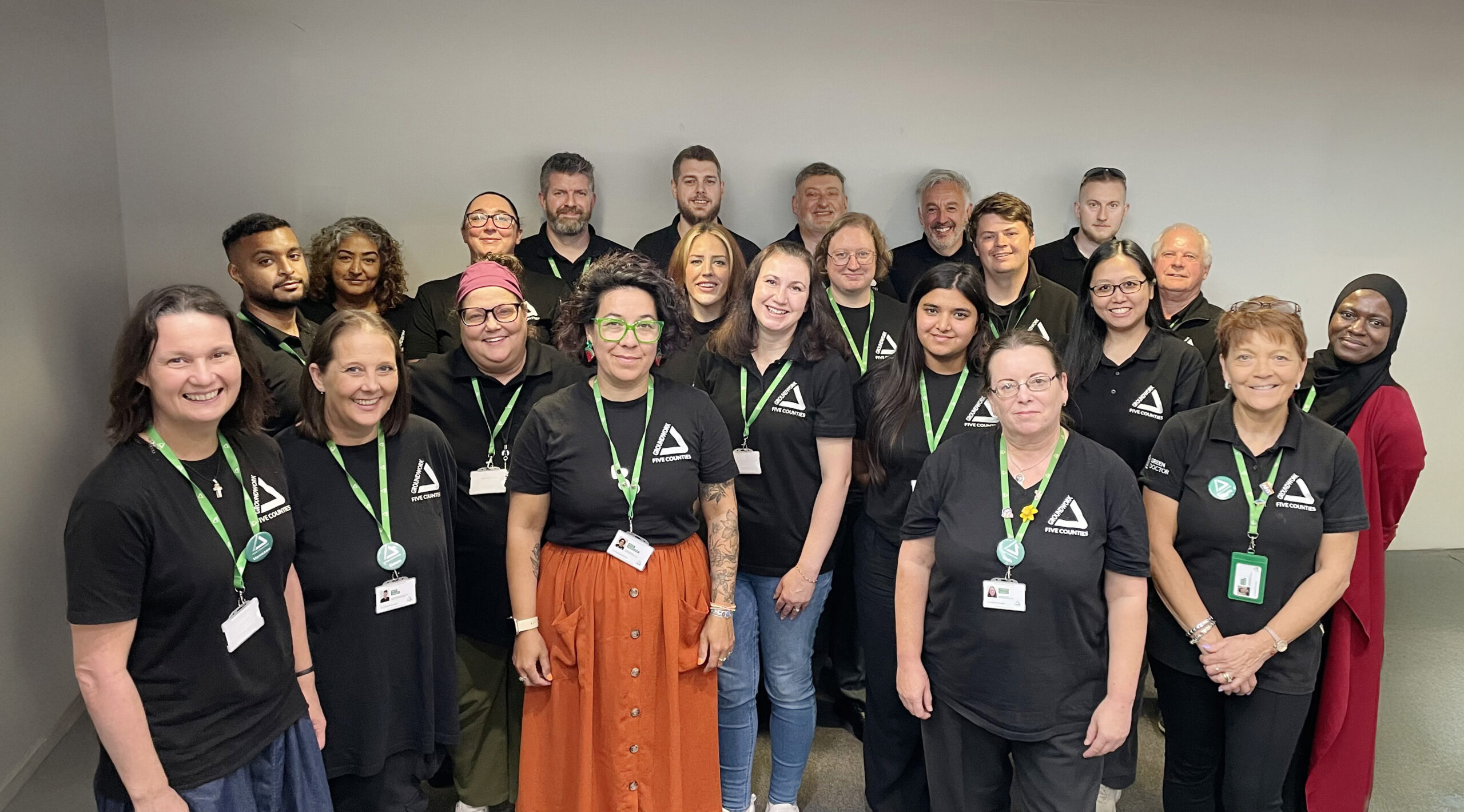 Group of people wearing black shirts and green lanyards smiling at camera.