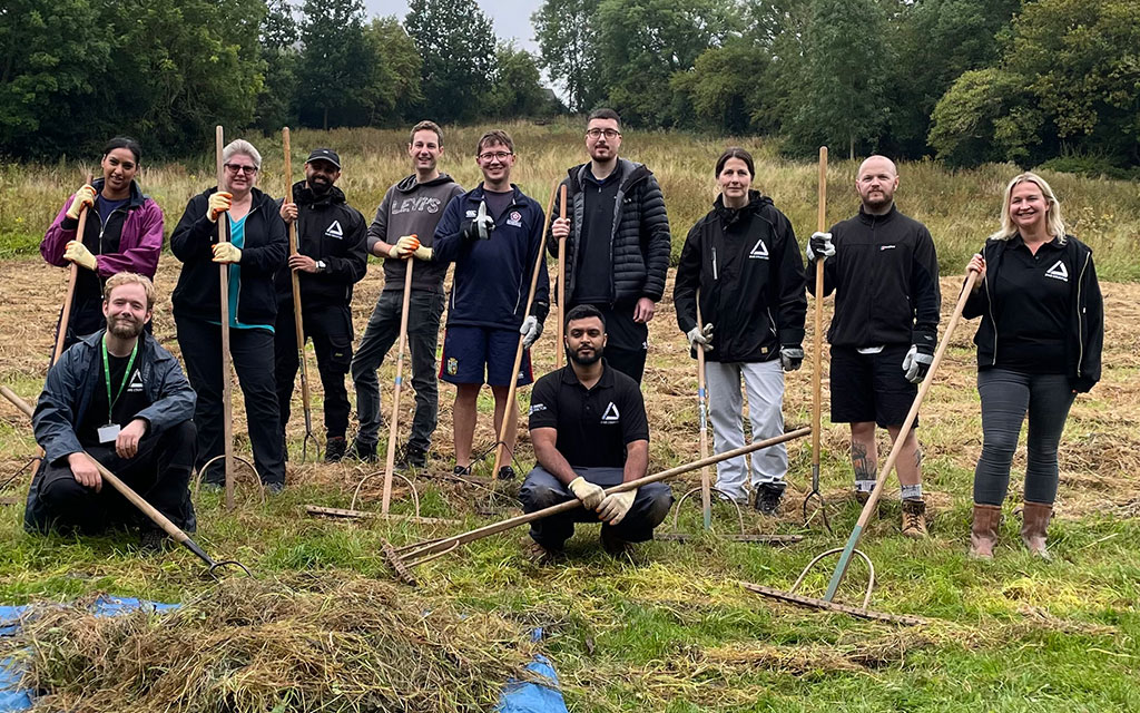 Group of people holding rakes and gardening tools in meadow.