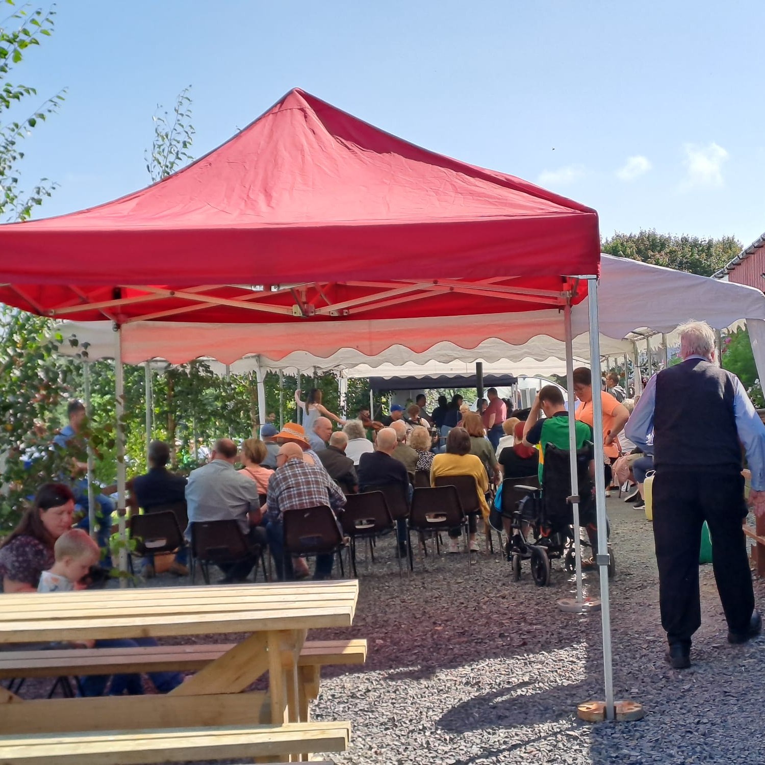 Lines of chairs filled with people under the shade of gazebo on a sunny day
