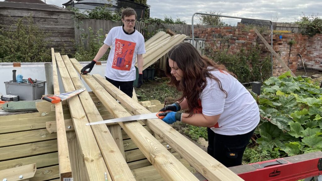 Young woman and man with planks of wood. The woman is holding a saw against wood.