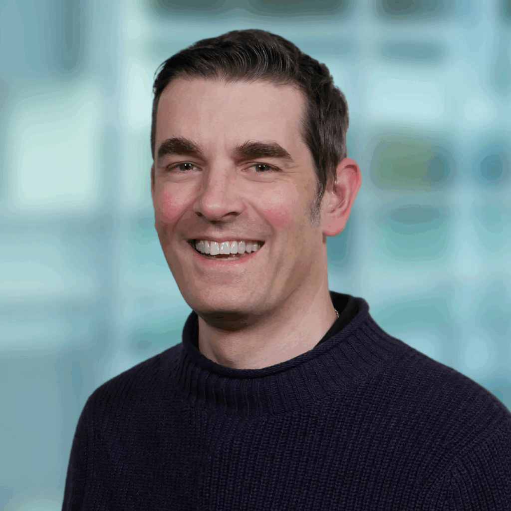 Man with short dark hair and black jumper smiling at camera