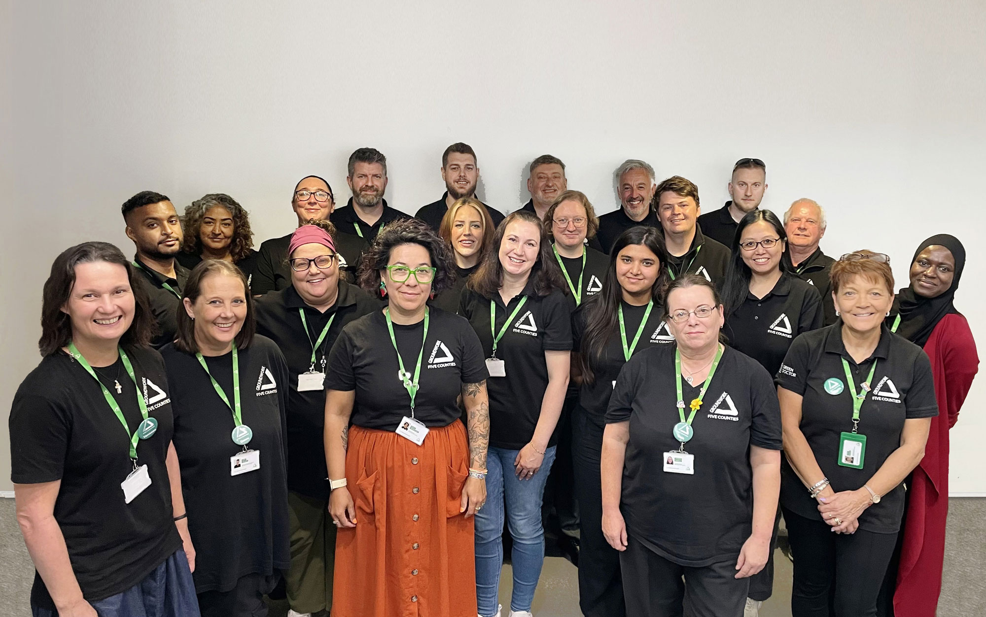 Group of people wearing black shirts and green lanyards smiling at camera.