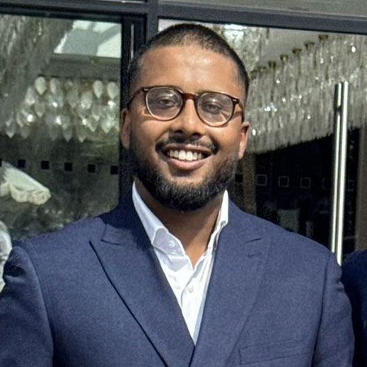 Man wearing glasses and dark blue suit jacket smiling at camera