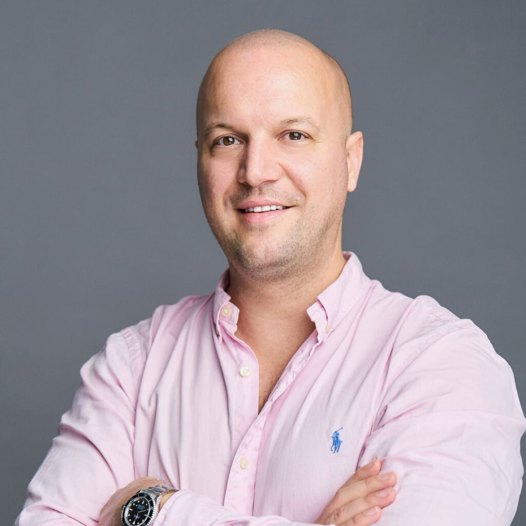 Bald man wearing light pink shirt with dark grey background