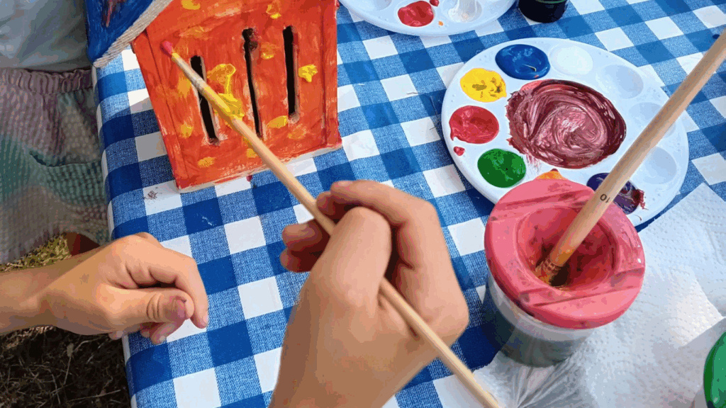 Hands painting a bird box on a table outside.