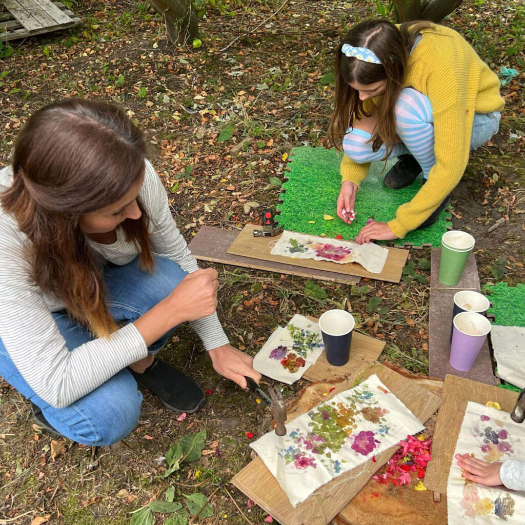 Two brunette woman making art with flowers on textile in outdoor setting