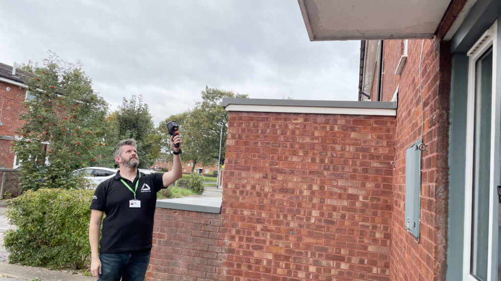Man holding thermal camera outside a home with red bricks
