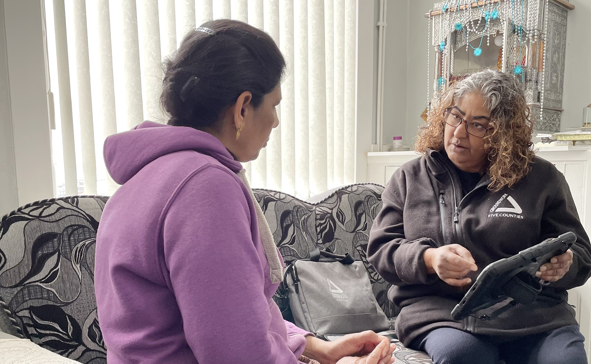 Two Asian women sitting on sofa talking to each other. One wears black, the other wears purple.