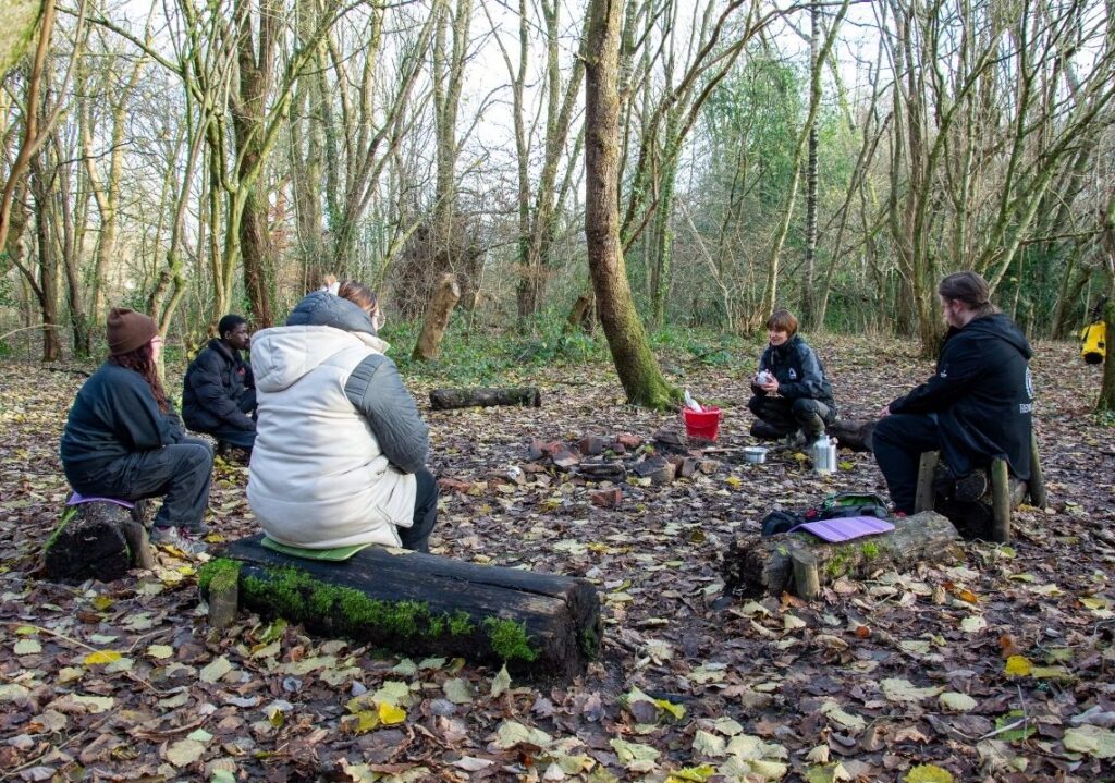 Young people taking part in alternative education around a campfire