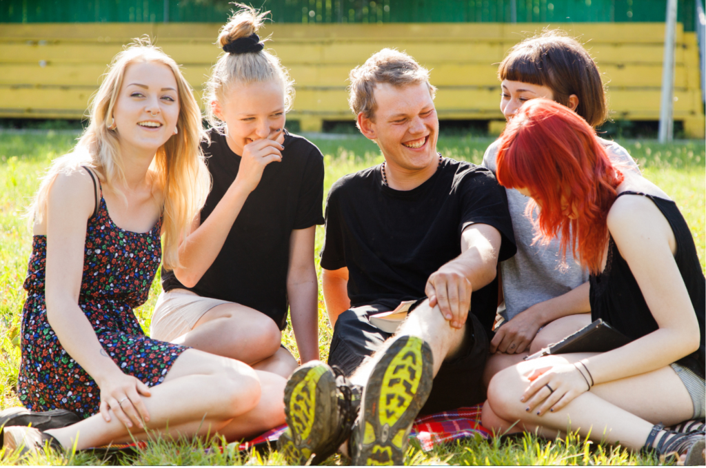 Teenagers sitting on the ground in the sunshine laughing