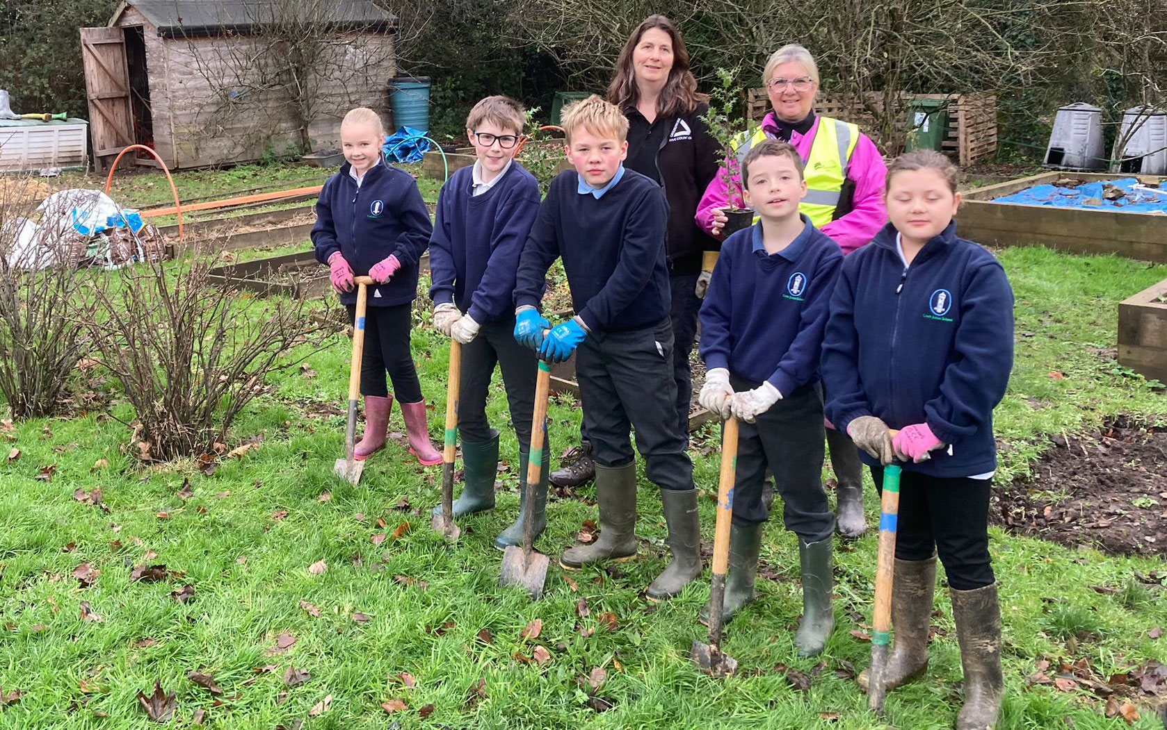 Group of children and two adults with shovels planting hedgerow whips.