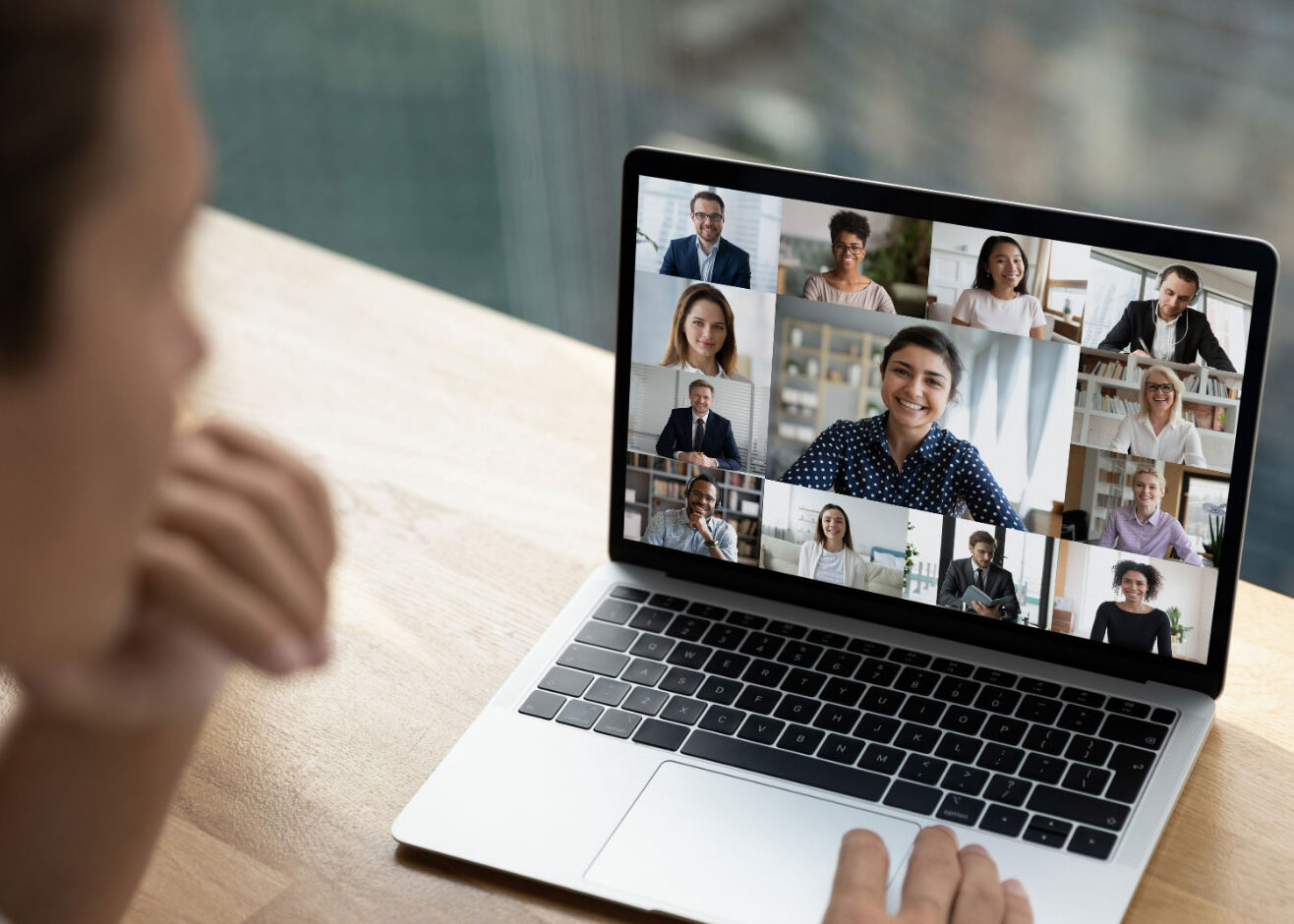 Person sitting at laptop in video call with multiple people on screen.