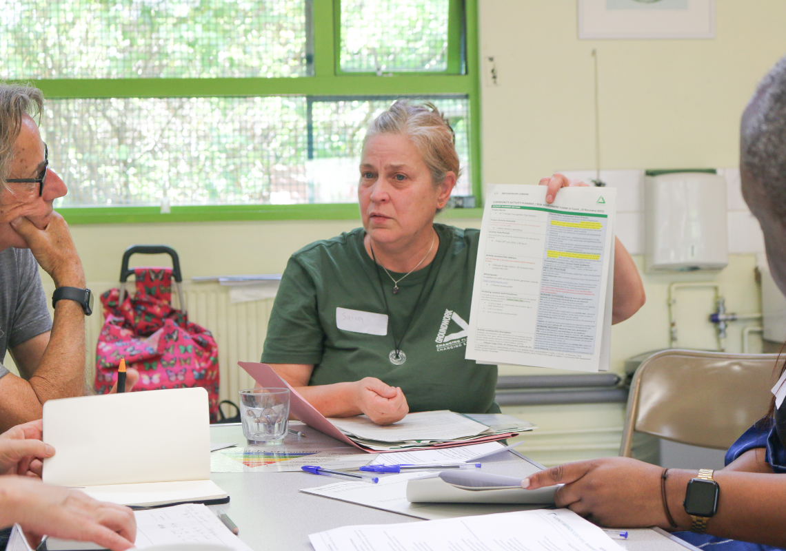 Image of a lady sat at a desk in a community centre holding a piece of paper
